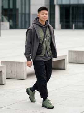 A pair of loose-fitting black cargo pants paired with a charcoal grey oversized hoodie and a matching olive green utility vest for a functional gorpcore look.