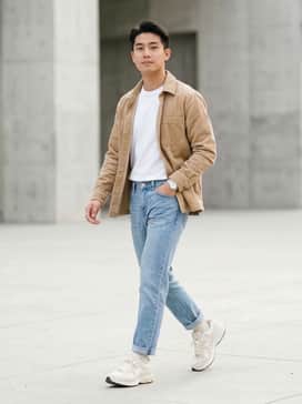 Straight-leg light wash denim jeans paired with a tucked-in white heavyweight cotton t-shirt and an unbuttoned tan corduroy shirt jacket.