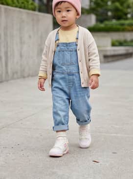 Light-wash denim dungarees worn over a soft yellow long-sleeve cotton tee, finished with a pink knit beanie to echo the sneaker's primary accents.