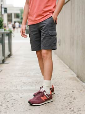 Charcoal grey cargo shorts matched with a coral-colored polo shirt to tie in with the bright accents on the sneakers for a coordinated weekend look.