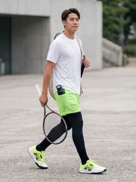 A performance-focused tennis ensemble featuring black compression tights under neon green mesh athletic shorts, paired with a fitted white moisture-wicking T-shirt for maximum court mobility.