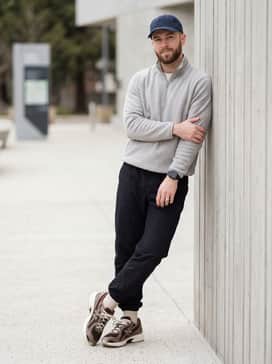 Relaxed black technical nylon joggers, a light grey quarter-zip fleece, and a navy blue baseball cap for a sport-inspired urban aesthetic.