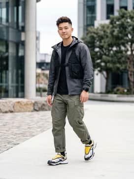 Acg Phassad – A 'Gorpcore' inspired outfit featuring olive green ripstop cargo pants, a black technical hardshell jacket, and a beige tactical vest for a layered outdoor look.