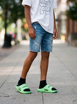 Mid-wash distressed denim shorts paired with an oversized white graphic t-shirt and a matching lime green baseball cap.