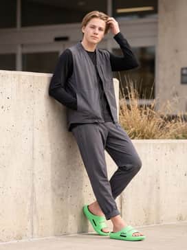 Charcoal grey tech-fleece joggers with a black utility vest over a long-sleeve mesh base layer for a futuristic streetwear vibe.