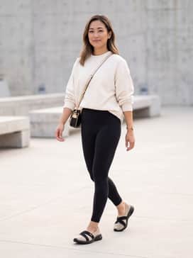High-waisted black leggings paired with an oversized cream-colored crewneck sweatshirt and a gold-accented crossbody bag.