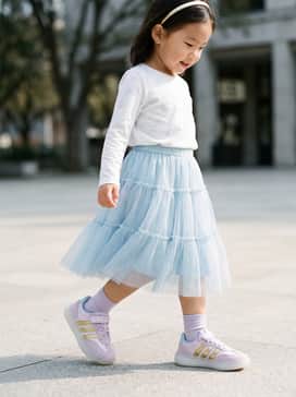 A whimsical Frozen-inspired look featuring a light blue tiered tulle skirt, a white long-sleeve tee with a subtle snowflake print, and a matching gold headband.