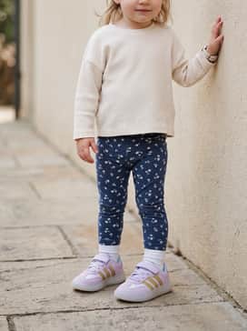 Adidas Disney Frozen Barreda Decode Shoes Children – A sporty casual ensemble with navy blue floral leggings, a cream-colored quilted puffer vest, and a simple grey jersey long-sleeve shirt.