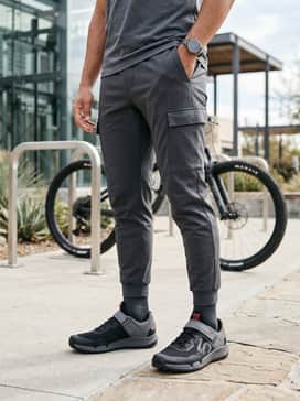 Dark charcoal tapered cargo joggers worn with a breathable olive green windbreaker and a moisture-wicking base layer for an urban outdoor aesthetic.