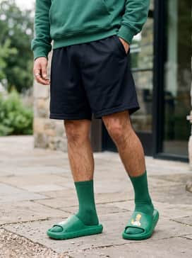 Adidas The Simpsons Adilette Lumia Slides – Oversized black mesh basketball shorts and a coordinating forest green hoodie to create a cohesive athleisure ensemble that focuses on comfort and bold color coordination.