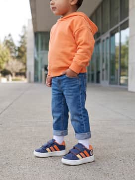 Adidas X Disney Mickey Mouse Grand Court Shoes Kids – Cuffed straight-leg denim jeans worn with a bright orange hoodie that echoes the vibrant stripes on the side of the shoe.