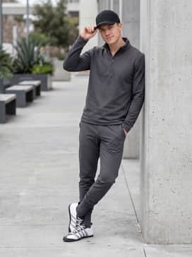 Tapered charcoal grey joggers worn with a matching technical quarter-zip pullover and a black baseball cap for a premium athleisure vibe.