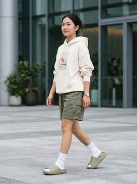 A cream-colored oversized graphic hoodie paired with olive cargo shorts and tall white crew socks for a trendy streetwear silhouette.