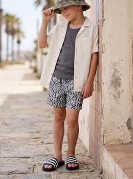 Wear with patterned swim trunks, a breathable linen short-sleeve button-down shirt left open over a tank top, and a bucket hat.