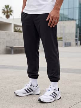 Slim-fit black joggers worn with a charcoal grey tech-fleece zip-up hoodie and high-performance white quarter socks to emphasize the athletic silhouette.