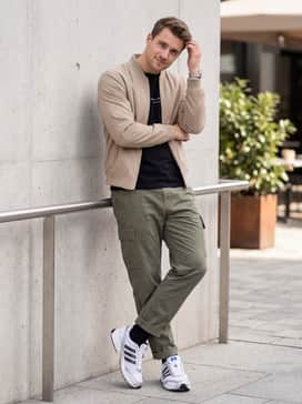 Olive green cargo pants with a tucked-in black graphic tee and a structured beige bomber jacket for a modern utility-inspired streetwear look.