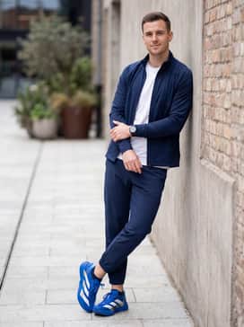 A sleek athleisure ensemble consisting of tapered navy blue tech joggers, a fitted white graphic tee, and a navy blue zip-up hoodie.