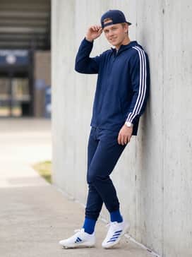 A sleek navy blue windbreaker with white racing stripes on the sleeves, paired with tapered navy joggers and a royal blue snapback cap for a coordinated pre-game look.