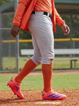 Adizero Electric 20 Shades Baseball Cleats – A summer tournament outfit featuring light grey performance knickers, high-top stirrup socks in a solid orange hue, and a breathable moisture-wicking graphic tee.
