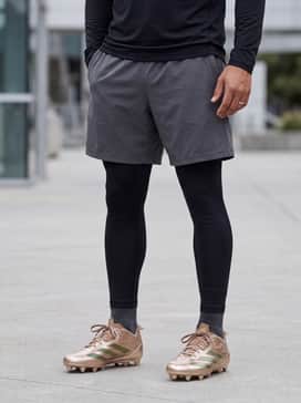 Black performance compression tights worn under charcoal grey athletic shorts, paired with a fitted black long-sleeve tech tee for a sleek practice ensemble.