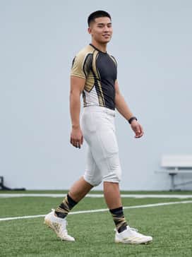 A full team-colored compression uniform featuring metallic gold accents and white padded football pants to highlight the shoe's sleek design.