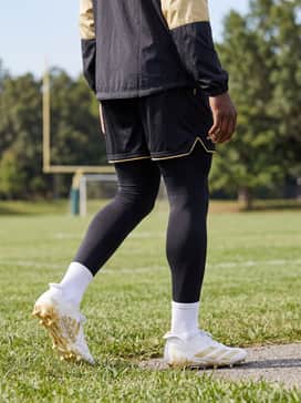 Adizero Electric Ii Smu Football Cleats – Black breathable training tights worn under mesh shorts with a matching black-and-gold windbreaker for cold-weather pre-game warm-ups.