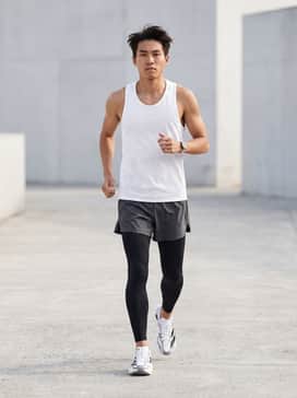 A professional running kit featuring black compression tights worn under charcoal split running shorts and a laser-cut white moisture-wicking singlet.