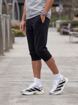 A sleek athleisure look with tapered black tech-fleece joggers, a grey fitted long-sleeve performance base layer, and a lightweight running gilet.