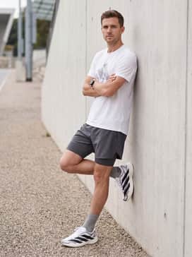 An urban training outfit consisting of 5-inch inseam athletic shorts in graphite, paired with a white oversized graphic tech-tee and high-performance quarter-length socks.