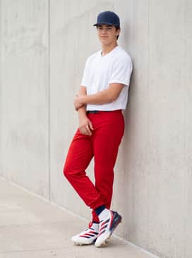 A high-contrast field ensemble with solid red baseball pants, a white breathable jersey, and a navy blue team-branded snapback cap.