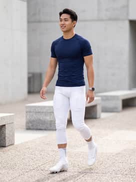 A professional game-day uniform consisting of white padded football pants, a navy blue compression-fit jersey, and white crew-length athletic socks for a streamlined look.