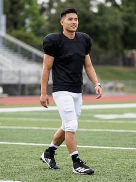 A full team uniform featuring a black mesh jersey, integrated padded football pants in white, and high-performance crew socks for a professional look.