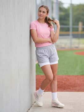 Light grey softball shorts worn over white sliding shorts with a matching pink team t-shirt for warm-weather training.