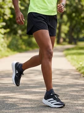 Summer training gear including 5-inch inseam black running shorts, a bright neon performance tee to contrast the monochrome shoes, and a matching headband.