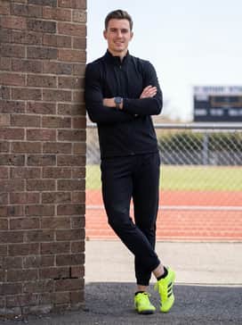 A coordinated black tracksuit featuring a slim-fit zip-up hoodie and tapered track pants with subtle reflective details to complement the neon shoes.