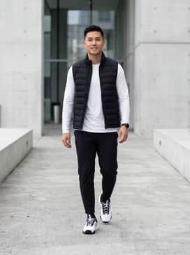 A monochromatic ensemble featuring black tapered joggers, a white long-sleeve performance base layer, and a black padded gilet for a sleek, athletic look.