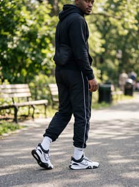 Black nylon track pants with white side-striping, worn with a tucked-in graphic hoodie and a minimalist crossbody bag for a modern streetwear edge.