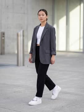 An oversized charcoal blazer paired with a white crop top and straight-leg black jeans, accessorized with silver rings to complement the sneaker's chain.
