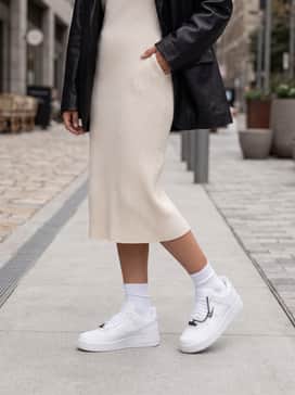 A cream-colored ribbed knit midi dress layered under an oversized black leather jacket for a balanced 'tough-meets-soft' aesthetic.