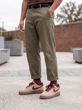 Olive green tapered cargo trousers worn with a black oversized graphic t-shirt and an unbuttoned flannel shirt in earth tones.