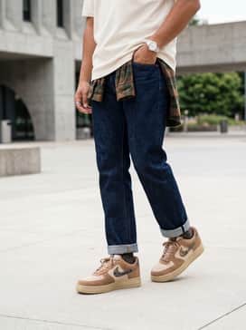 Air Force 1 07 Realtree – Dark indigo raw denim jeans with a significant cuff, worn with a white heavyweight t-shirt and a flannel shirt in shades of brown and forest green.