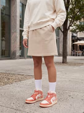 Air Jordan 1 Mid – A beige tennis skirt matched with a vintage graphic sweatshirt and high-top white socks to lean into the 'varsity' trend.