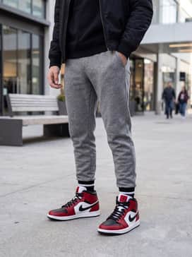 Air Jordan 1 Mid – Tapered heather grey joggers combined with a black fitted hoodie and a neutral-toned bomber jacket to make the bold red colorway pop.