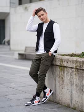 Style with dark olive cargo pants and a black tactical vest over a long-sleeve white tee for a rugged streetwear look.