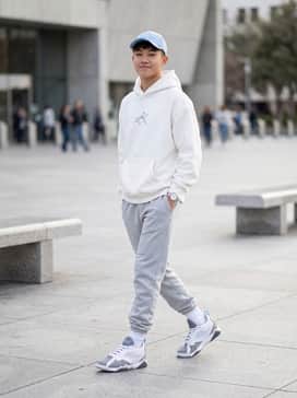 Light grey fleece joggers paired with a matching oversized white hoodie and a light blue baseball cap to mirror the shoe's accents.