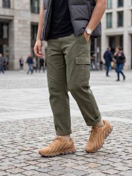 Air Max Dn8 Leather – Olive green cargo pants with adjustable hems, worn with a black mock-neck tech-fabric shirt and a charcoal puffer vest.