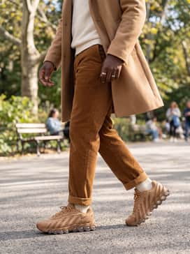 Tobacco-colored corduroy trousers with a slight crop, a tucked-in off-white knit sweater, and a camel overcoat for a sophisticated monochromatic ensemble.