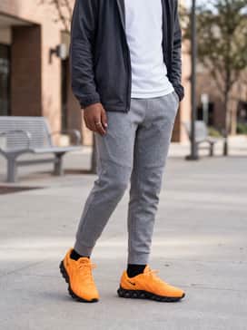 A neutral-toned athletic look with heather grey tech fleece sweatpants, a white performance t-shirt, and a grey zip-up windbreaker.