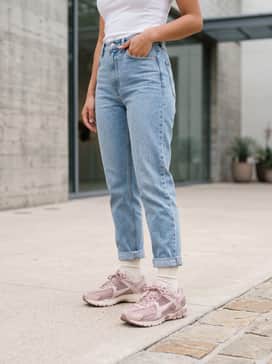 Light-wash high-waisted mom jeans paired with a fitted white baby tee and a vintage-style denim jacket, accessorized with a small nylon shoulder bag and chunky silver hoop earrings.