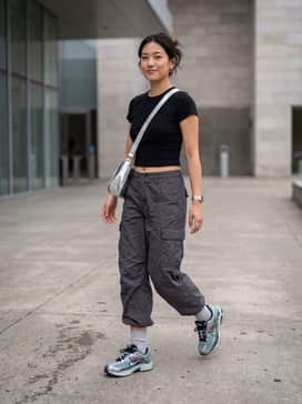 Baggy charcoal cargo pants paired with a black cropped baby tee and a silver metallic shoulder bag for a complete Y2K street look.